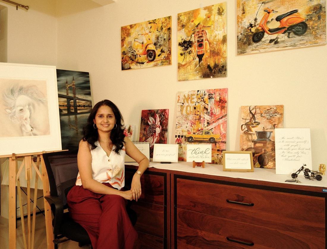 Vinda Shinde seated in her studio in front of a wall of her colourful abstract realism paintings