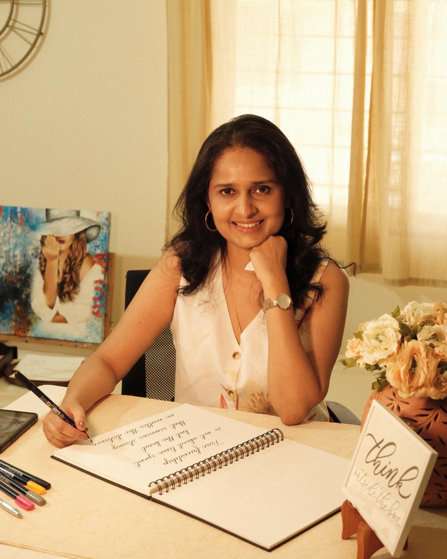 Vinda Shinde smiling at her desk, writing calligraphy in a notebook